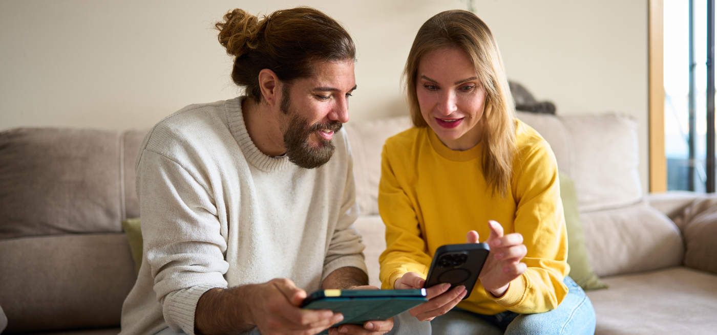 Casal a comparar informação num tablet e telemóvel, sentados no sofá